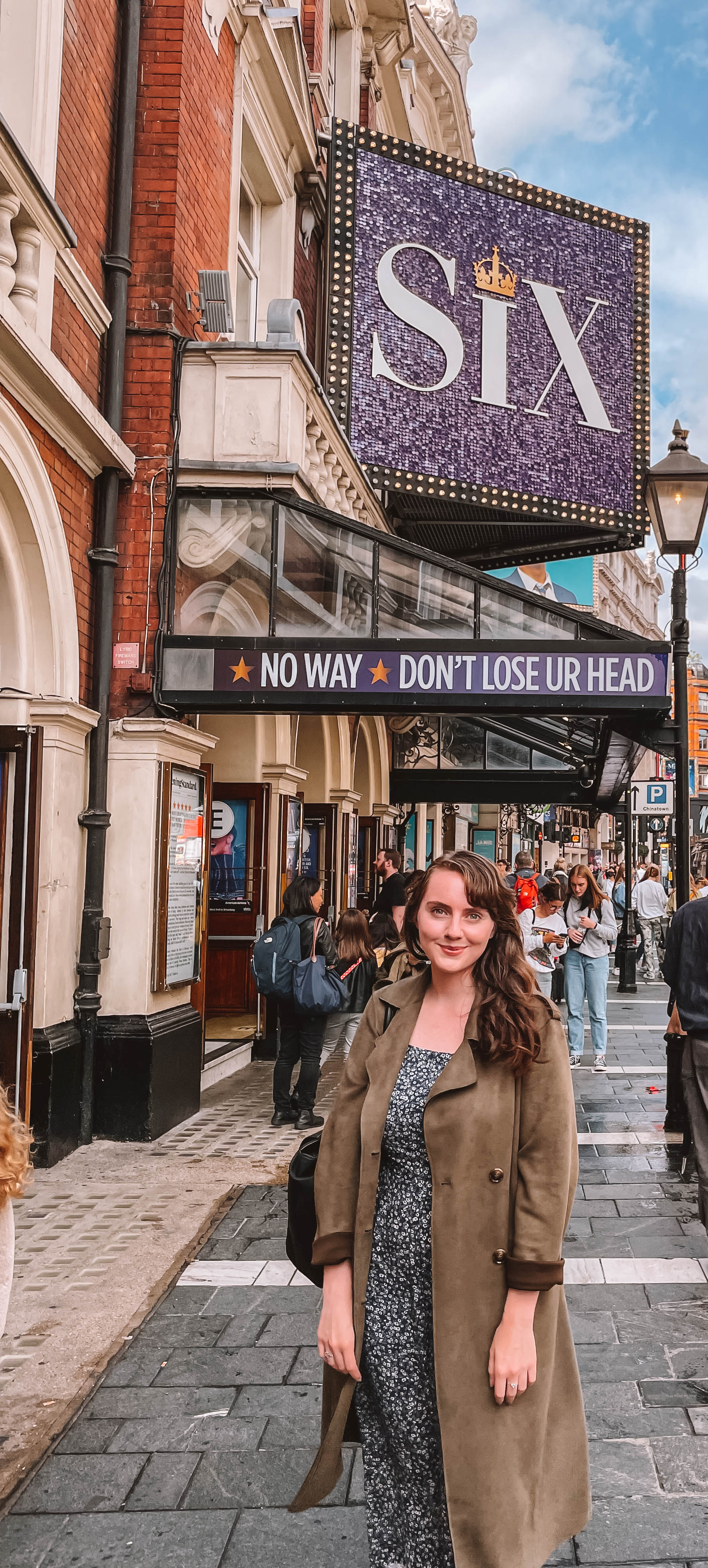 A woman standing in front of a theater sign that is advertising for SIX the musical